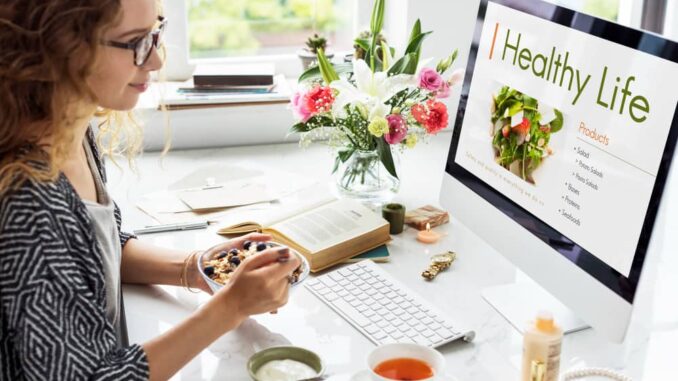 Femme prenant un petit-déjeuner sain devant son ordinateur pour trouver des solutions bien-être au quotidien sans dépasser son budget.