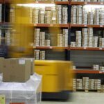 Un chariot jaune déplace des palettes de cartons dans un entrepôt