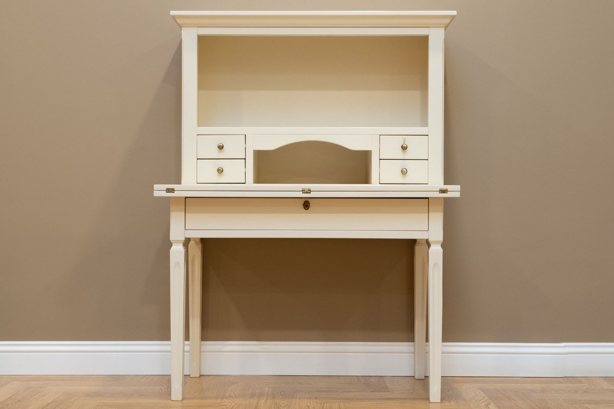 Un bureau pliant blanc avec tiroirs et niche, posé contre un mur beige Un bureau pliant blanc avec tiroirs et niche, posé contre un mur beige