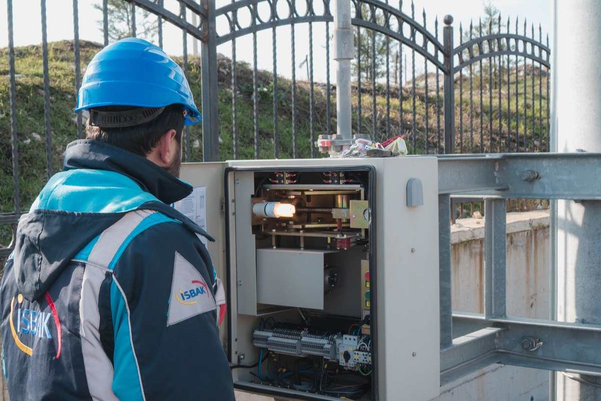 Technicien examine un équipement électrique en extérieur près d'une clôture