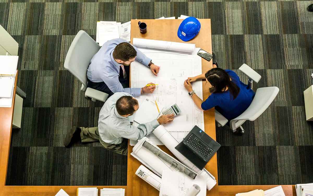 Trois collaborateurs analysent des plans sur un bureau Trois collaborateurs analysent des plans sur un bureau