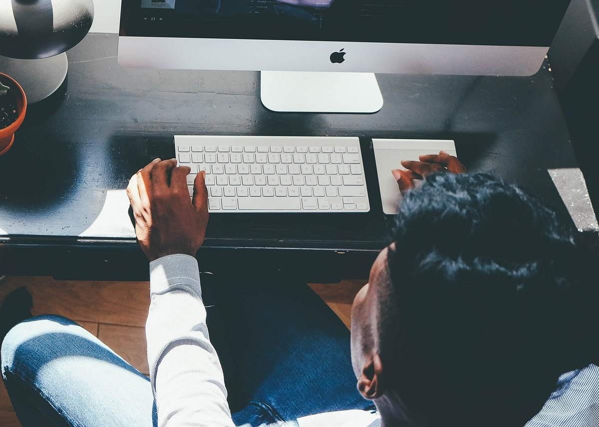 Un homme travaille sur un ordinateur iMac, clavier et souris